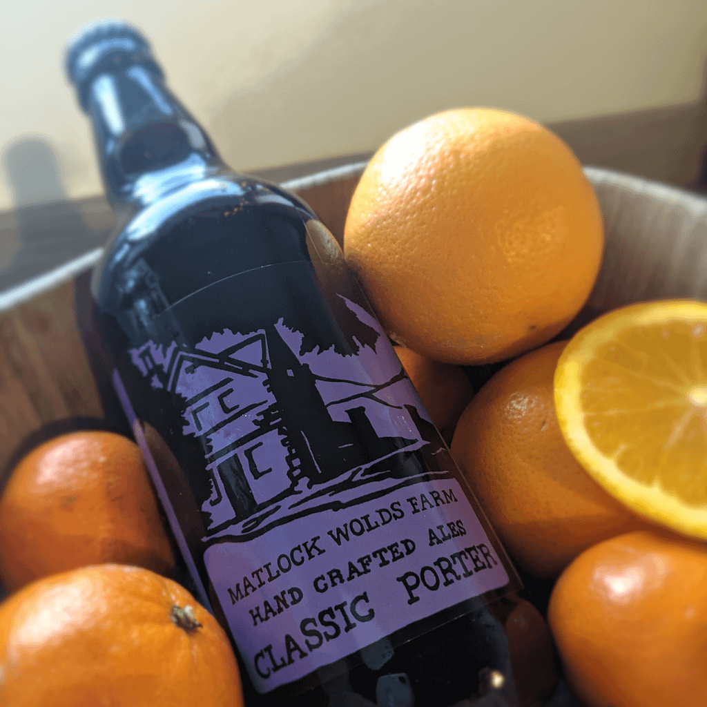 A bottle of Matlock Wolds Farm Classic Porter in a bowl amongst several oranges
